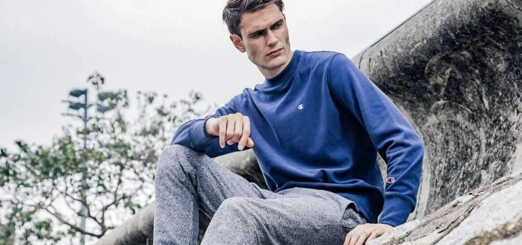 Pria mengenakan sweater lengan panjang berwarna biru, dengan celana panjang berwarna abu-abu.